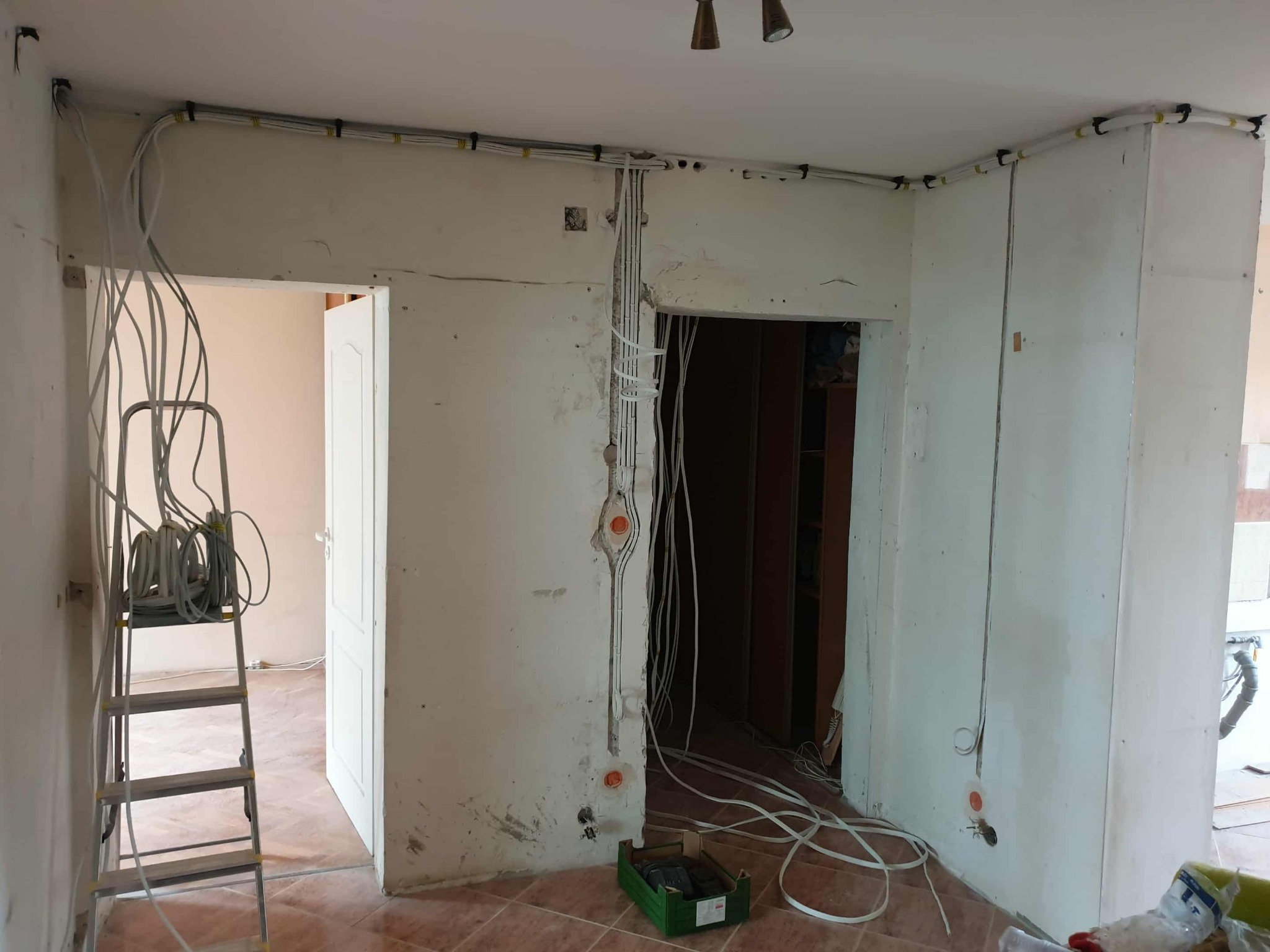 Wnętrze w trakcie remontu z widoczną instalacją elektryczną: kable prowadzone po ścianach i suficie, puszki elektryczne. Na podłodze narzędzia i drabina.