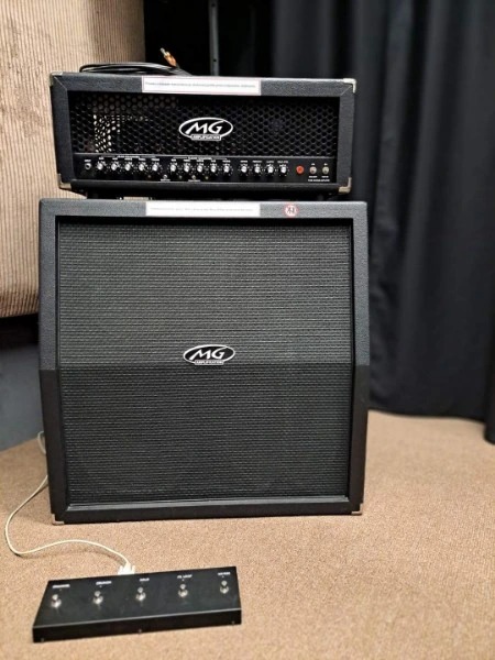 Zestaw wzmacniacza gitarowego MG z kolumną i przełącznikiem nożnym, ustawiony na brązowej podłodze w pomieszczeniu z zasłonami w tle.