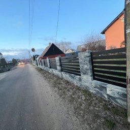 Taras Malena - Nowoczesne ogrodzenie panelowe z elementami imitującymi kamień, widoczne z perspektywy ulicy w pochmurny dzień. W tle domy i przejeżdżający samochód.