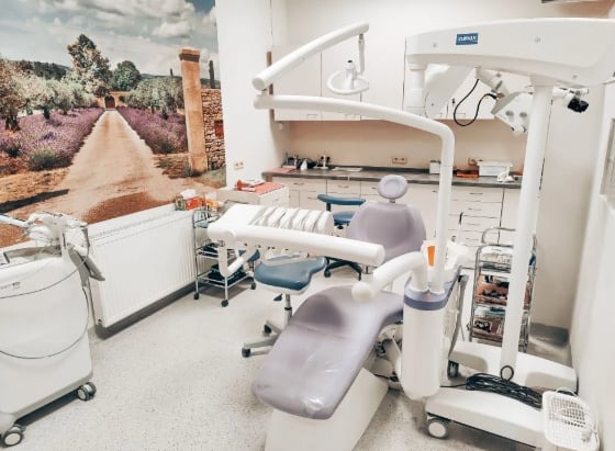 Nowoczesny gabinet stomatologiczny z fotelem w odcieniach fioletu, lampą zabiegową, laserem stomatologicznym i fototapetą z motywem toskańskim.