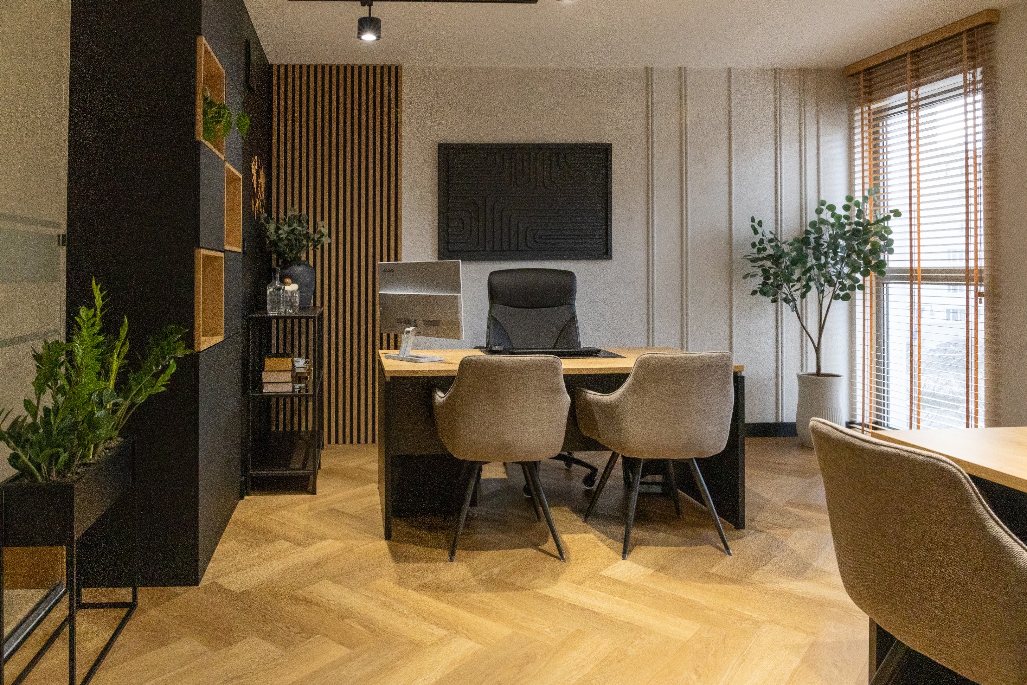 Nowoczesne biuro z drewnianą podłogą w jodełkę, czarnymi akcentami i roślinami. Biurko z komputerem i krzesłami, minimalistyczny design, naturalne światło z okna.