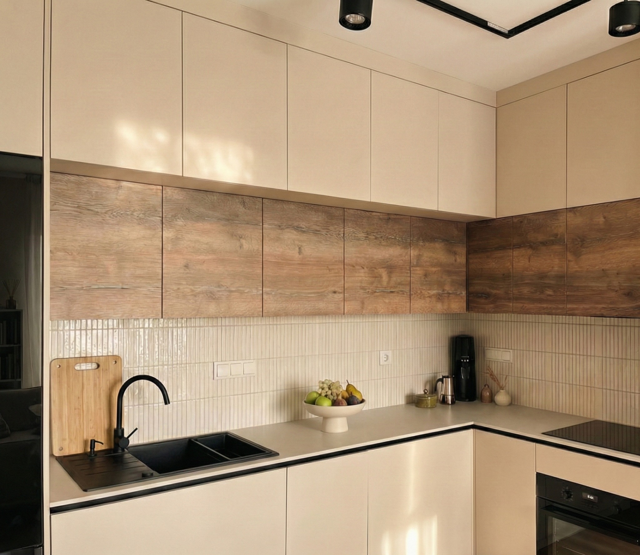 Nowoczesna kuchnia w odcieniach kaszmiru i orzecha z drewnianymi szafkami górnymi, czarnym zlewem i armaturą. Na blacie misa z owocami i akcesoria kuchenne.