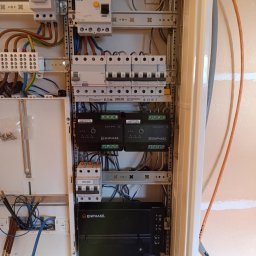 Remigiusz Ulanowski KASREM ELEKT - Rozdzielnica elektryczna z zainstalowanymi modułami Enphase, bezpiecznikami Legrand i Eaton. Widoczne przewody i listwy zaciskowe. Całość w białej obudowie.