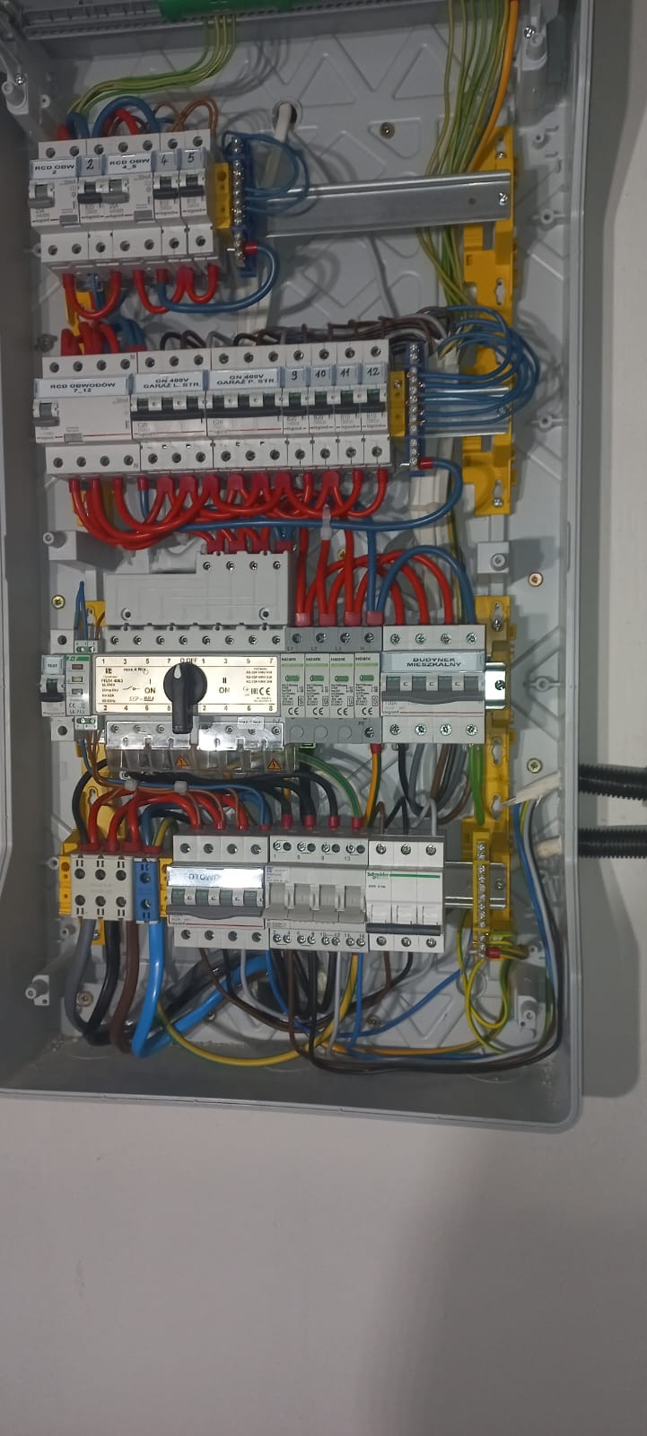 Rozdzielnica elektryczna z bezpiecznikami i okablowaniem w szarej obudowie, zamontowana na ścianie. Realizacja z Olecka.