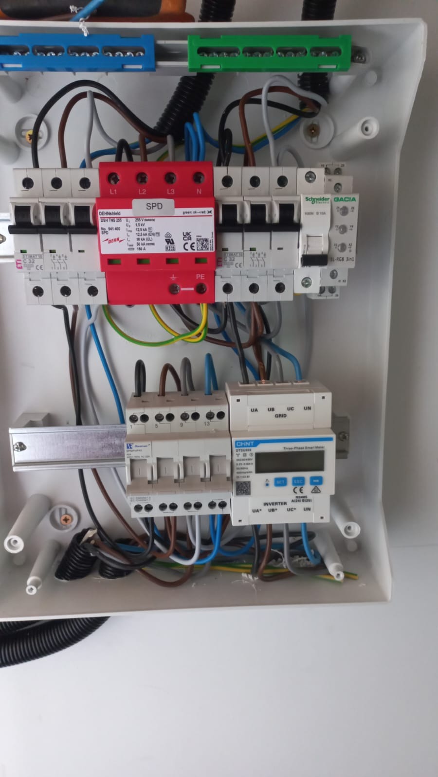 Wnętrze skrzynki elektrycznej z zamontowanym modułem SPD (ochrona przeciwprzepięciowa), bezpiecznikami i licznikiem energii. Widoczne okablowanie i listwy zaciskowe.