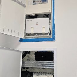Szuba Volt System - Otwarta skrzynka rozdzielcza z bezpiecznikami, routerem Fiberway, TP-Link i multiswitchem Signal MP-0908. Widoczne kable i lista kontrolna na drzwiach.