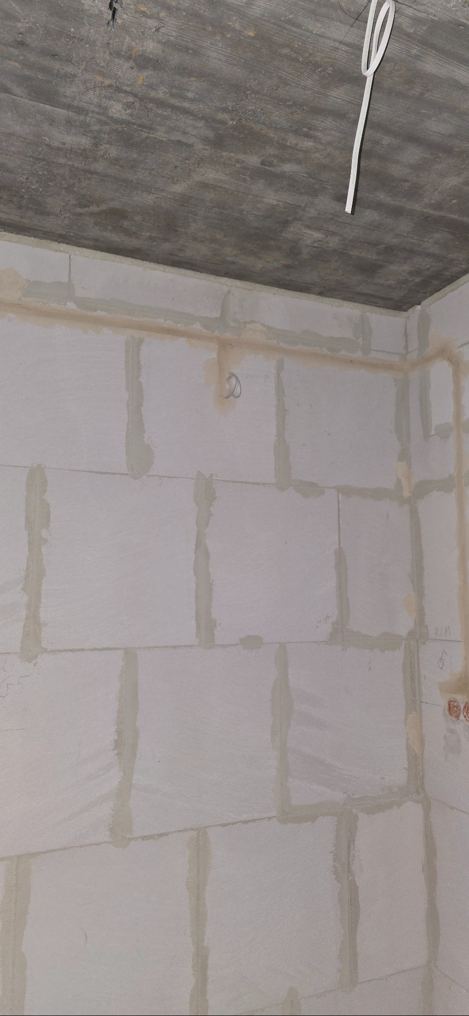 Surowa ściana z betonu komórkowego z widocznymi przewodami elektrycznymi wystającymi z sufitu, przygotowana do dalszych prac wykończeniowych.