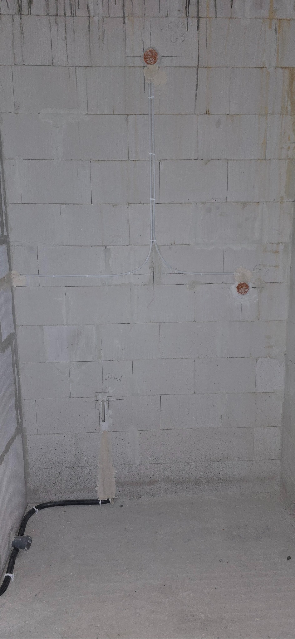 Surowa ściana z betonu komórkowego z widocznymi przewodami elektrycznymi w peszlach i puszkami instalacyjnymi, przygotowana do dalszych prac wykończeniowych.