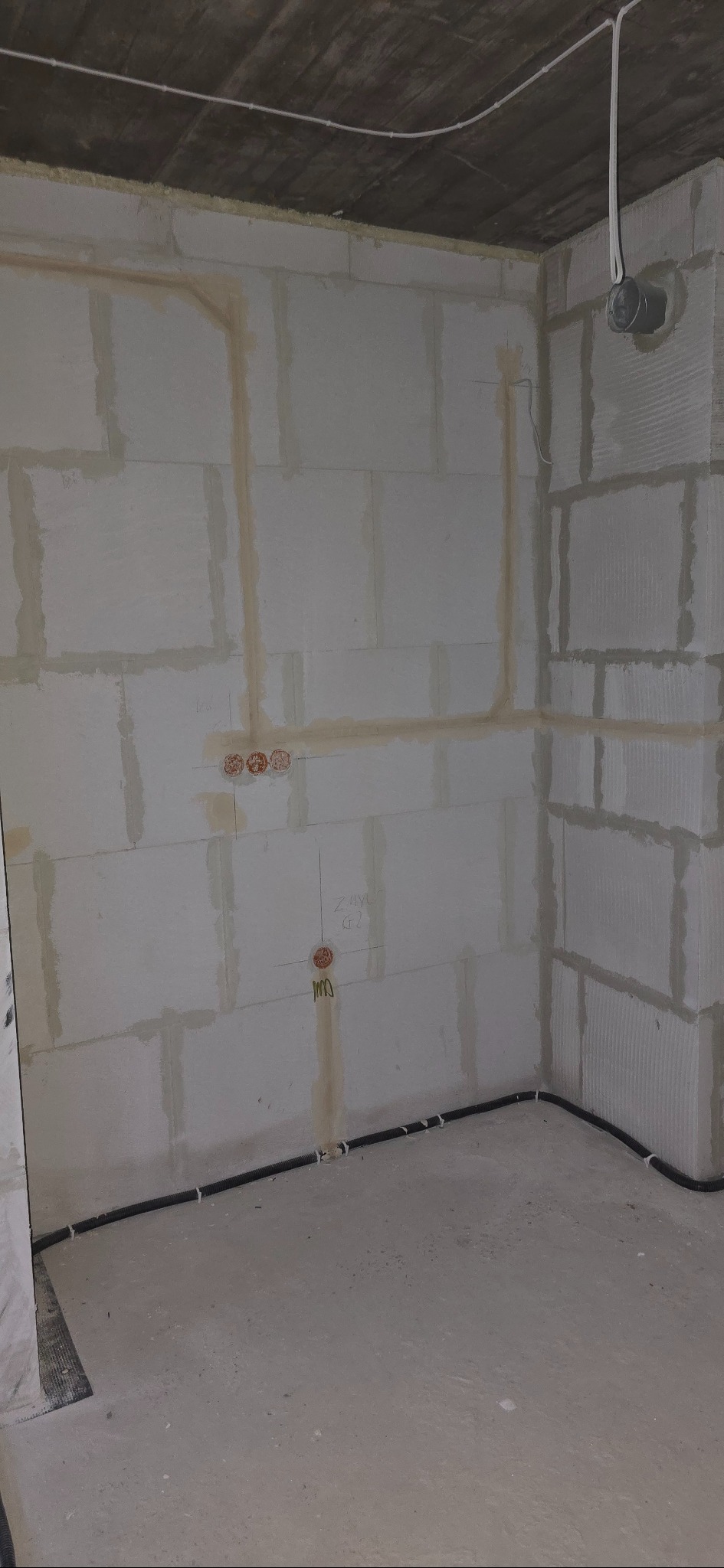 Surowy pokój z widocznymi przewodami elektrycznymi w ścianach i pod sufitem, przygotowany do dalszych prac wykończeniowych. Widoczne puszki pod gniazdka.