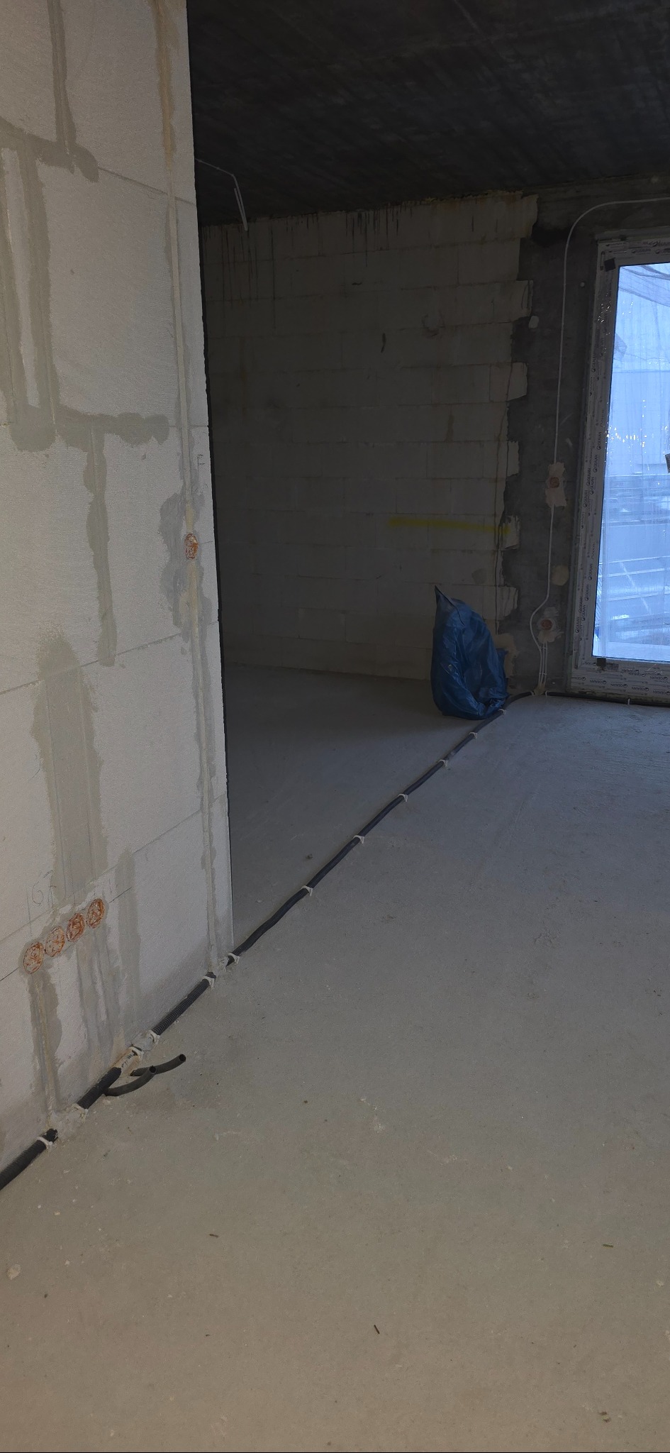 Surowy stan: kable elektryczne ułożone wzdłuż ściany w nowym budynku, widoczne puszki instalacyjne w ścianie z betonu komórkowego, okno w tle.