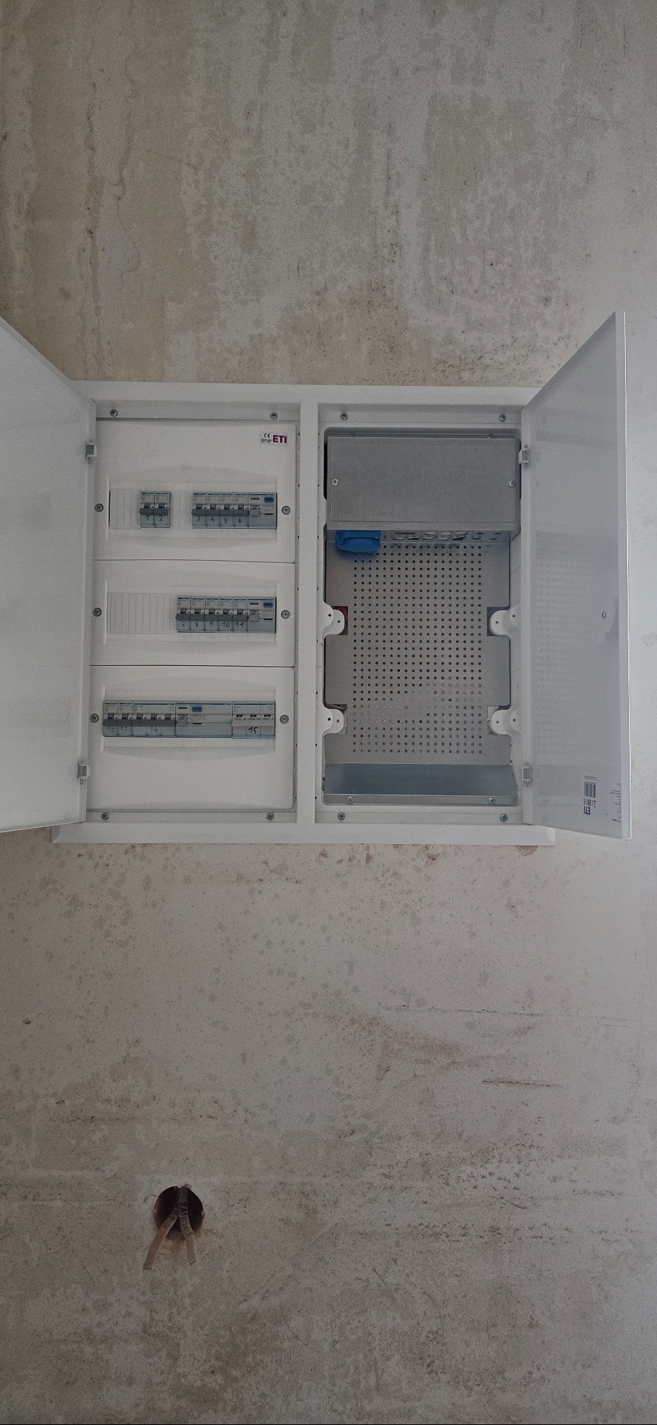 Otwarta skrzynka bezpiecznikowa z zainstalowanymi bezpiecznikami na szarej ścianie w Borzęcinie. Widoczne kable i elementy instalacji.