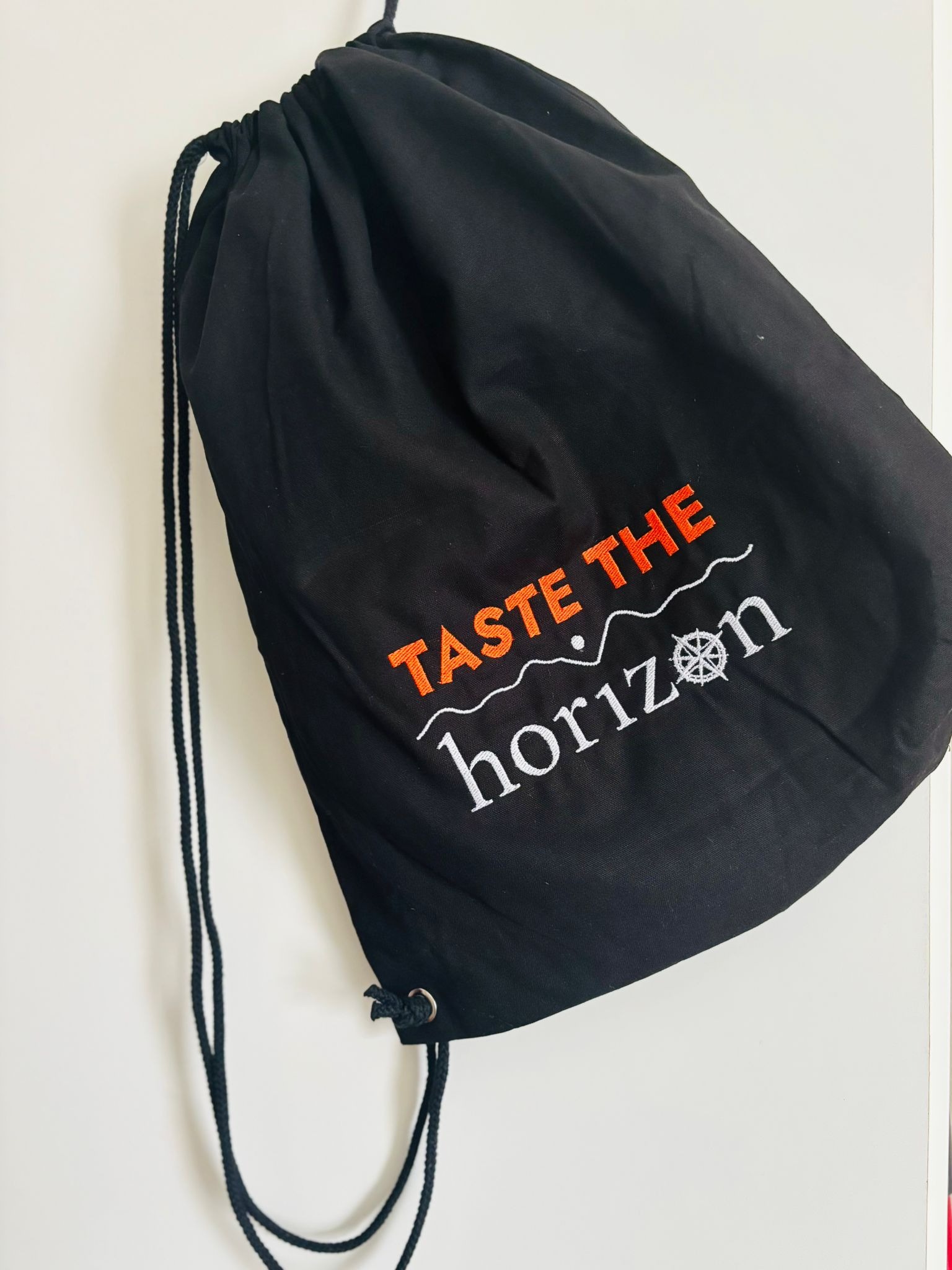 Czarny worek z haftowanym napisem 'Taste the horizon' w pomarańczowo-białej kolorystyce, ukazujący detale wykonania i estetykę projektu.