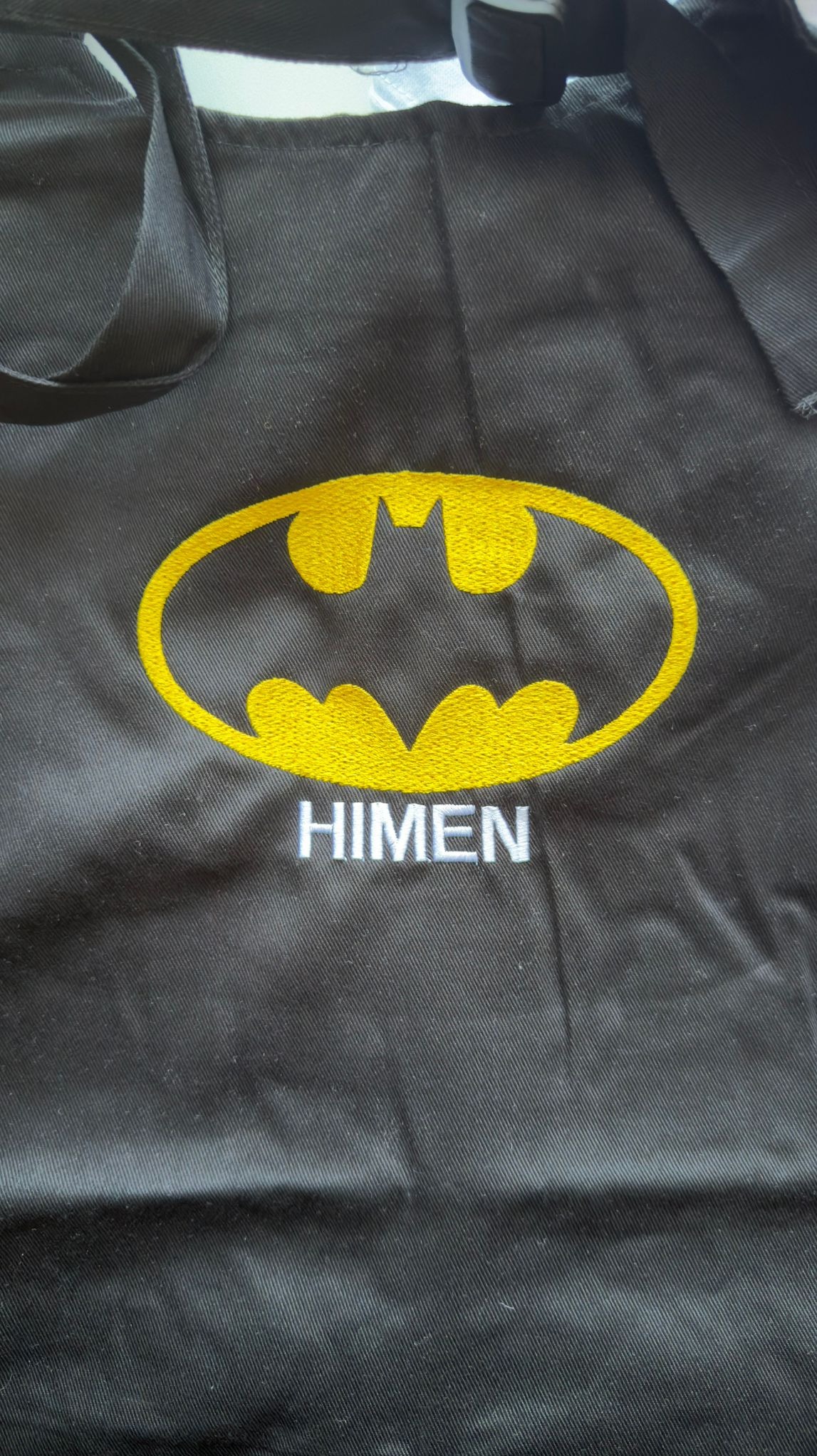 Czarna torba z żółtym haftem logo Batmana i białym napisem 'HIMEN' pod spodem, wykonana techniką haftu komputerowego.