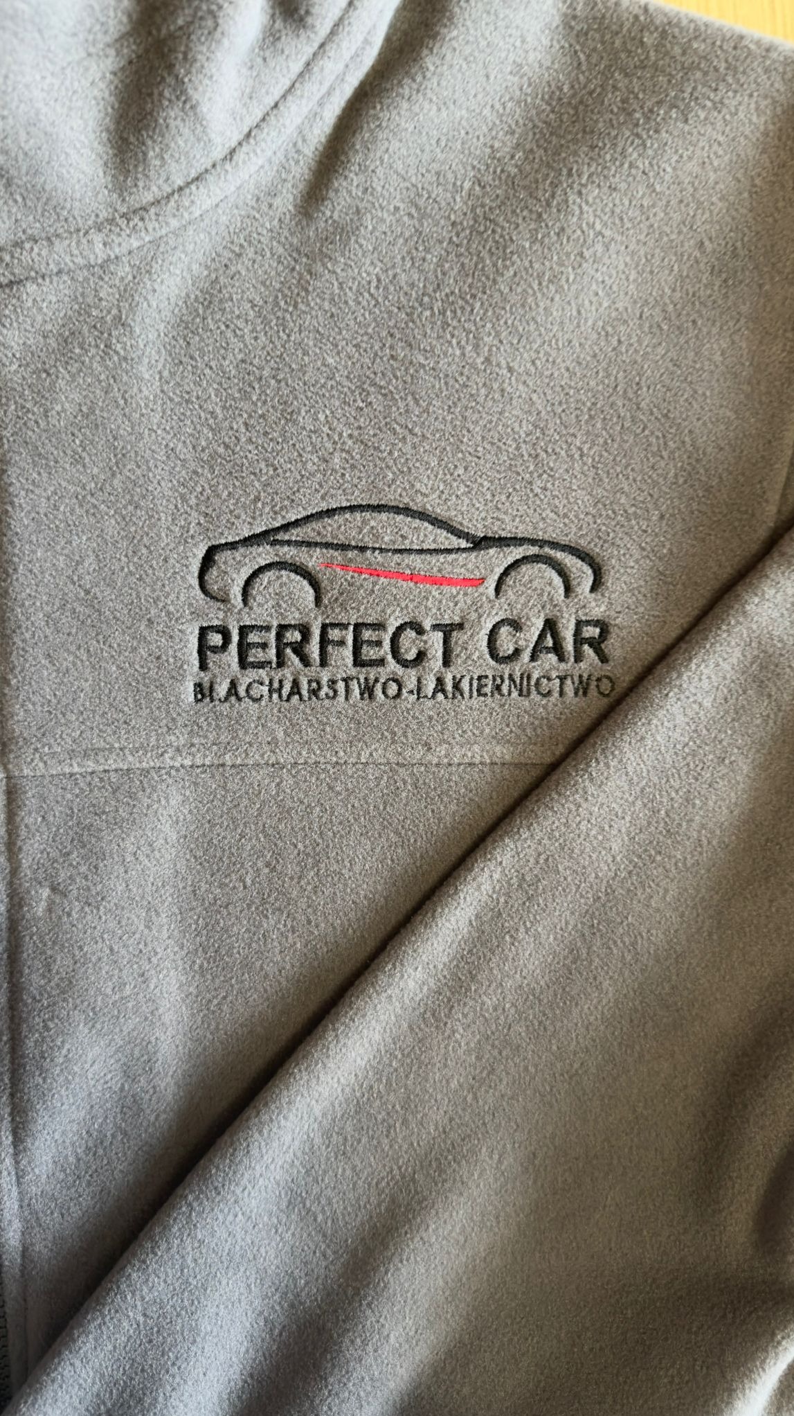 Szara bluza polarowa z wyhaftowanym logo firmy 'Perfect Car' (blacharstwo-lakiernictwo). Widoczne detale haftu i faktura materiału.