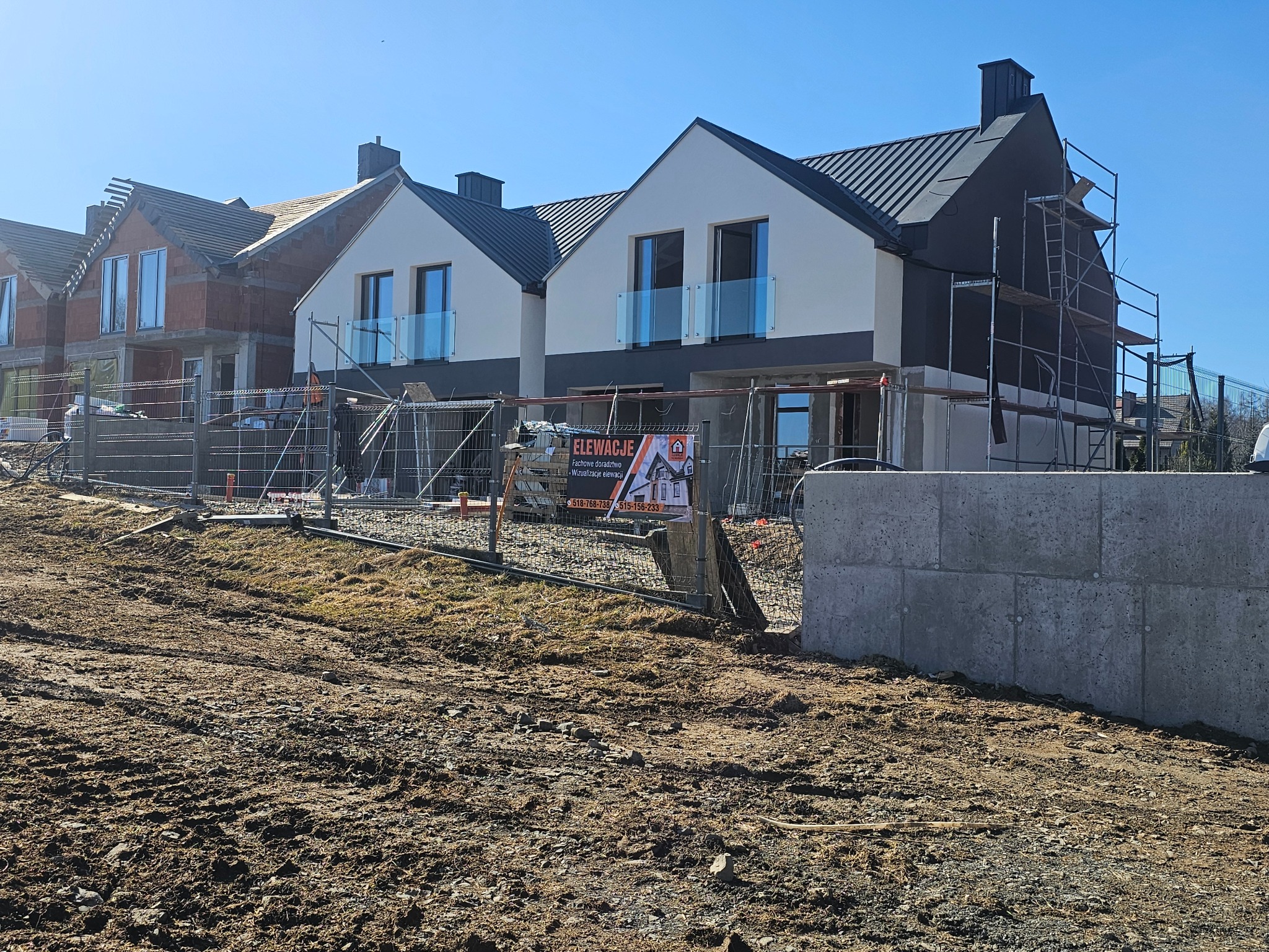 Domy w zabudowie szeregowej w trakcie prac elewacyjnych: jeden w stanie surowym, drugi z ocieploną biało-grafitową elewacją i szklanymi balustradami, trzeci z rusztowaniem przy ciemnej elewacji...