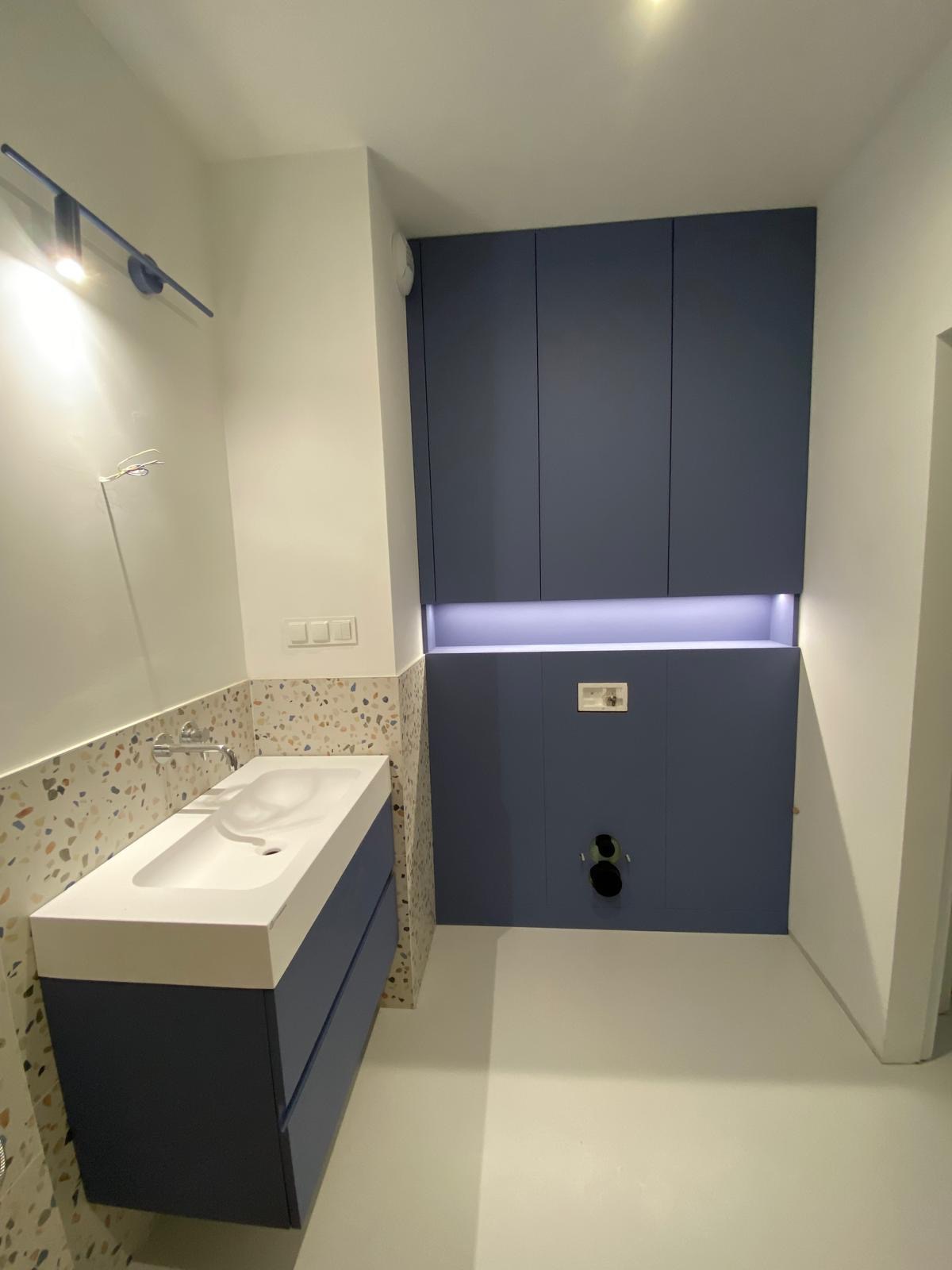 Nowoczesna łazienka z umywalką nablatową na szafce w odcieniach granatu, mozaikową ścianą i zabudową podtynkową z oświetleniem LED.
