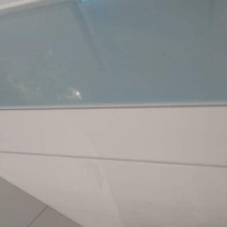 MUR-BETON - Położona glazura w łazience, jasne, poziome płytki z wąską fugą. U góry fragment błękitnej ściany. Ujęcie z dołu, widoczne delikatne odbicia światła na powierzchni płytek.