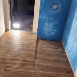 Układanie płytek imitujących drewno na podłodze w łazience z niebieską hydroizolacją na ścianach. Widoczny odpływ liniowy.