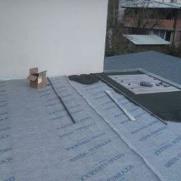 MUR-BETON - Montaż warstwy izolacyjnej Delta-Terraxx na balkonie z widokiem na dach budynku. Widoczne narzędzia i karton. Prace w toku.