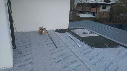 Montaż warstwy izolacyjnej Delta-Terraxx na balkonie z widokiem na dach budynku. Widoczne narzędzia i karton. Prace w toku.