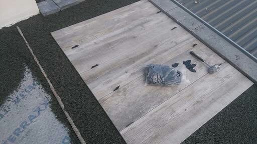 Układanie płytek imitujących drewno na dachu z zielonym podłożem. Obok leżą narzędzia i akcesoria montażowe. Widoczny fragment membrany dachowej.