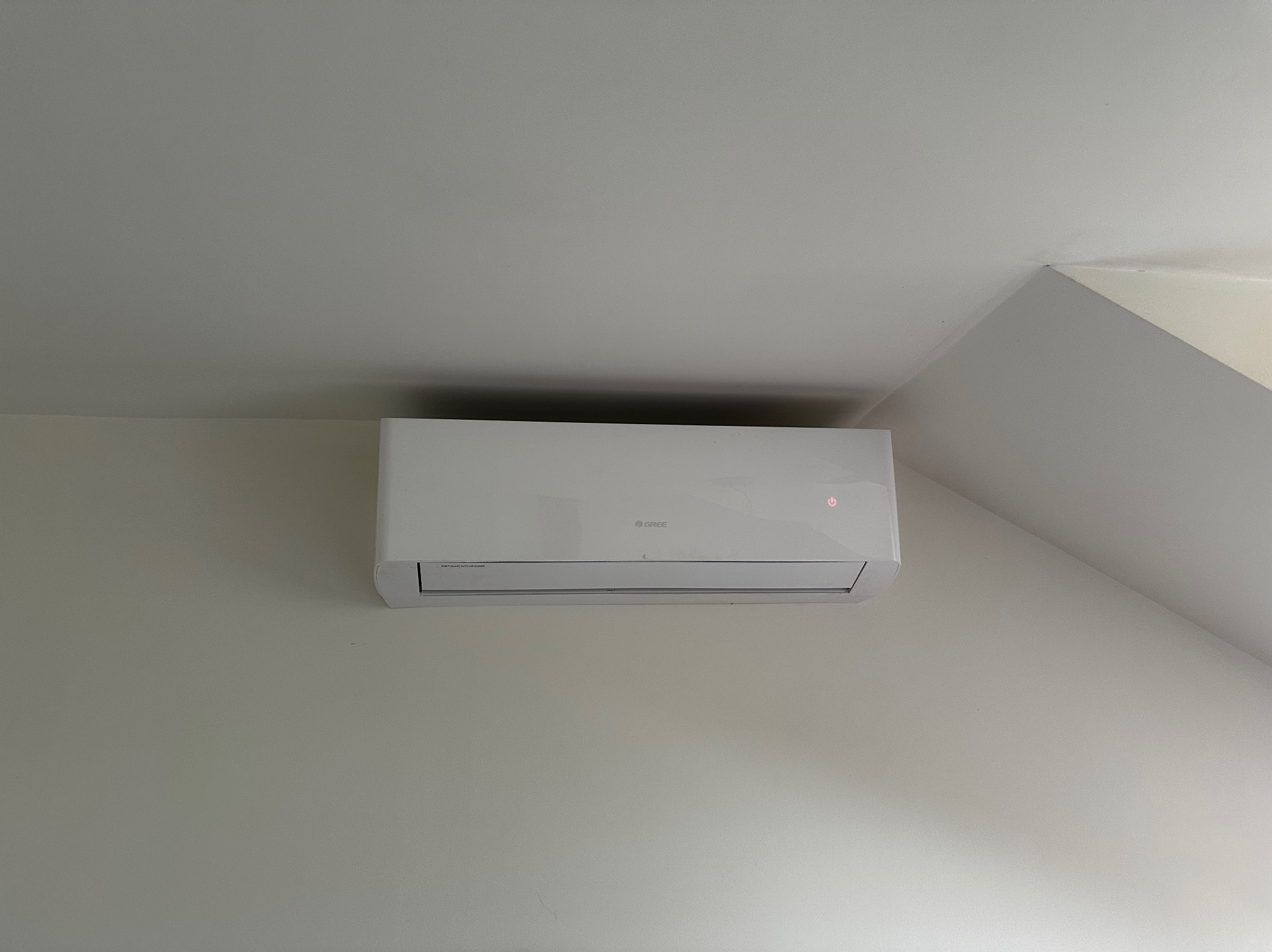 Biała klimatyzacja Gree zamontowana na jasnej ścianie w pomieszczeniu ze skośnym sufitem.