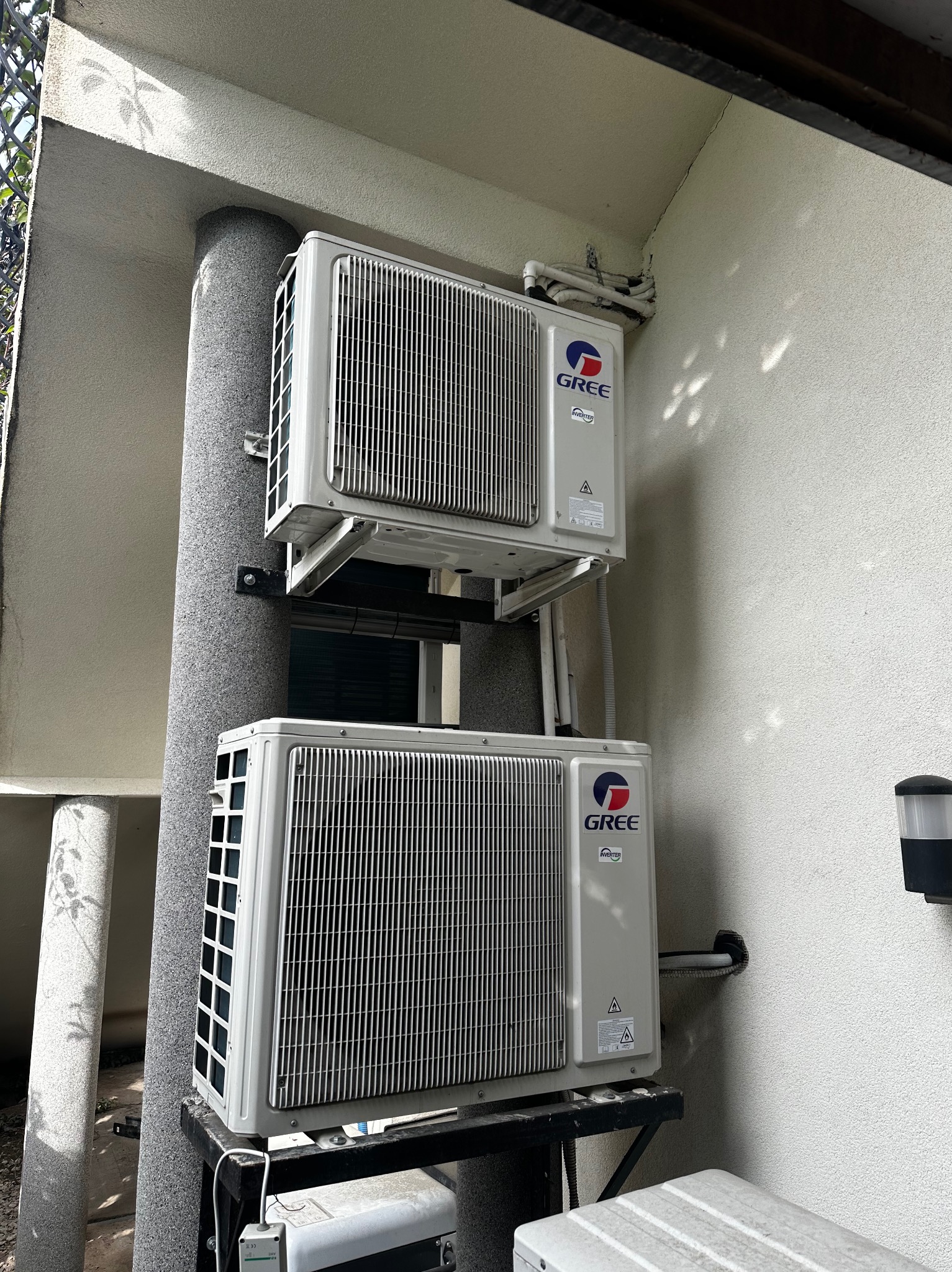 Dwa białe klimatyzatory marki Gree zamontowane jeden nad drugim na zewnątrz budynku, z widocznymi rurami i elementami montażowymi.