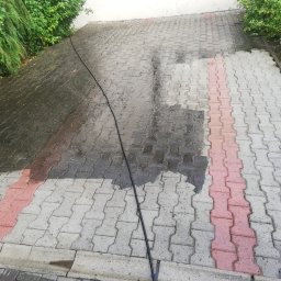 Mycie maszynowe - Częściowo umyta kostka brukowa z widocznym wężem ciśnieniowym, ukazująca różnicę w czystości między umytą a nieumytą powierzchnią.