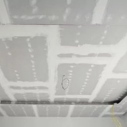 Mycie maszynowe - Sufit podwieszany z płyt gipsowo-kartonowych w trakcie szpachlowania, widoczne łączenia płyt i wystające przewody elektryczne.