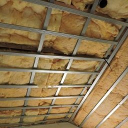 Mycie maszynowe - Skośny sufit poddasza w trakcie ocieplania wełną mineralną, widoczna metalowa konstrukcja nośna i fragment ściany.