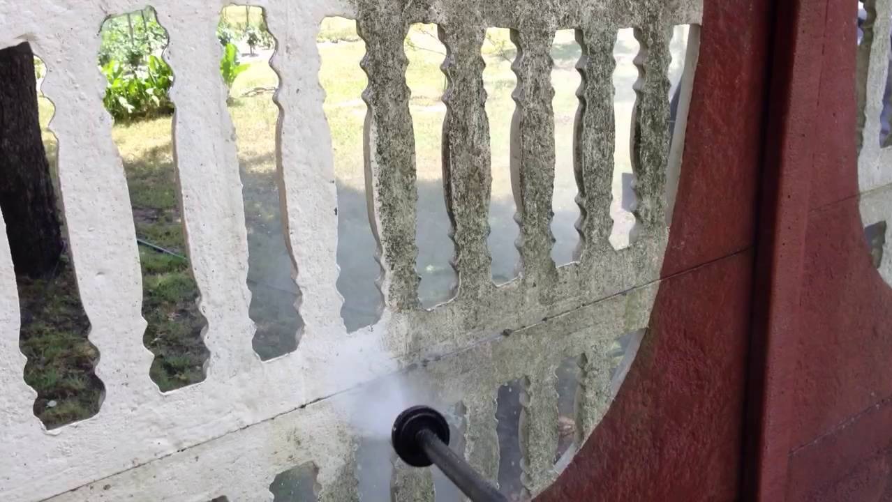 Czyszczenie ciśnieniowe betonowego ogrodzenia z ażurowymi przęsłami, widoczne różnice w kolorze przed i po czyszczeniu, fragment czerwonego słupka ogrodzeniowego po prawej.