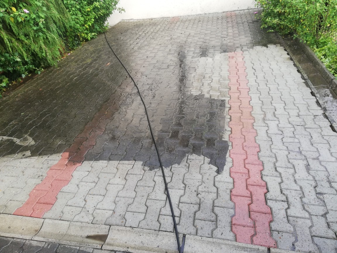 Częściowo umyta kostka brukowa z widocznym wężem ciśnieniowym, ukazująca różnicę w czystości między umytą a nieumytą powierzchnią.