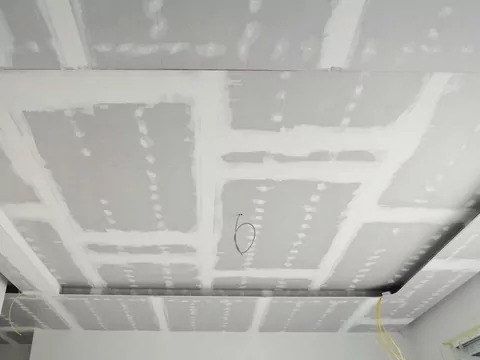 Sufit podwieszany z płyt gipsowo-kartonowych w trakcie szpachlowania, widoczne łączenia płyt i wystające przewody elektryczne.