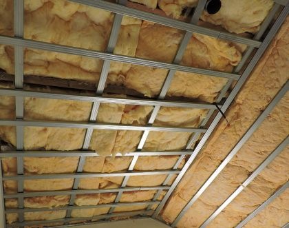 Skośny sufit poddasza w trakcie ocieplania wełną mineralną, widoczna metalowa konstrukcja nośna i fragment ściany.