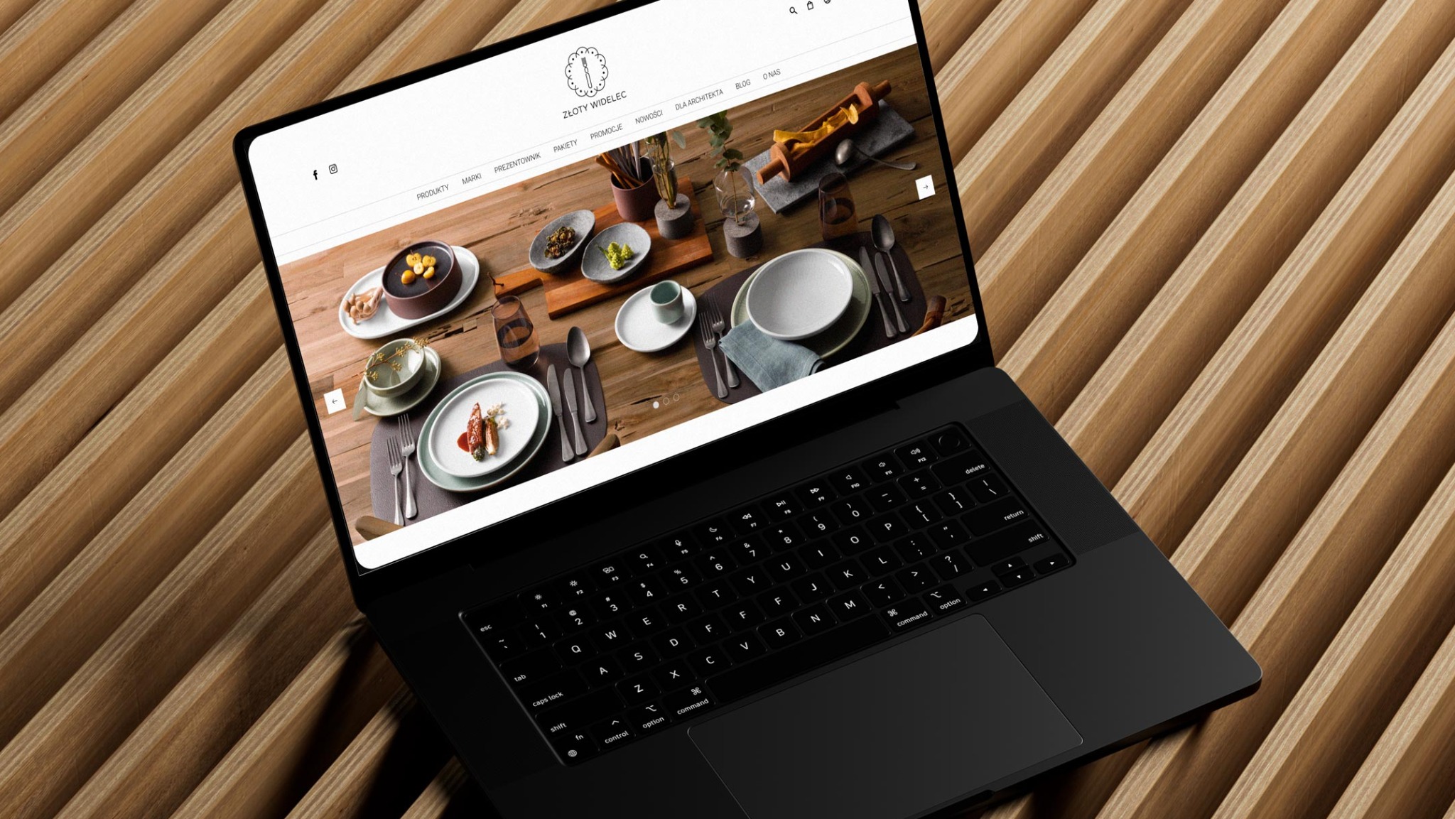 Czarny laptop na drewnianym tle prezentuje stronę internetową z aranżacjami stołów i naczyń, widoczne logo 'Złoty Widelec' w górnej części ekranu.