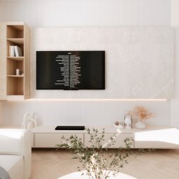 Kwiatkowska Studio - Jasne wnętrze salonu z minimalistyczną szafką RTV, telewizorem wyświetlającym napisy końcowe filmu, dekoracjami i rośliną w doniczce. Na ścianie marmurowa okładzina i oświetlenie LED.