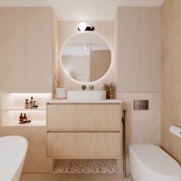 Kwiatkowska Studio - Jasna łazienka z drewnianą szafką pod umywalką, okrągłym lustrem z podświetleniem LED, ukrytą półką z kosmetykami i toaletą.