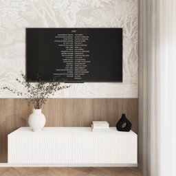 Kwiatkowska Studio - Telewizor z wyświetlonymi napisami końcowymi filmu, umieszczony na tle ściany z tapetą w motywy drzew i drewnianą boazerią. Poniżej biała szafka RTV z wazonem z gałązkami i czarnym, dekoracyjnym...