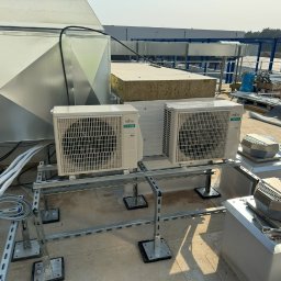 EkoKlima Montaż klimatyzacji - Dwa zewnętrzne moduły klimatyzacji Fujitsu Airstage zamontowane na metalowej konstrukcji na dachu budynku, widoczne białe rury i kanały wentylacyjne.