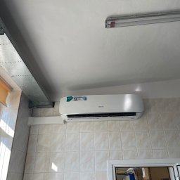 EkoKlima Montaż klimatyzacji - Biały klimatyzator Hisense zamontowany na kafelkowanej ścianie, widoczny kanał wentylacyjny i okno z roletą.