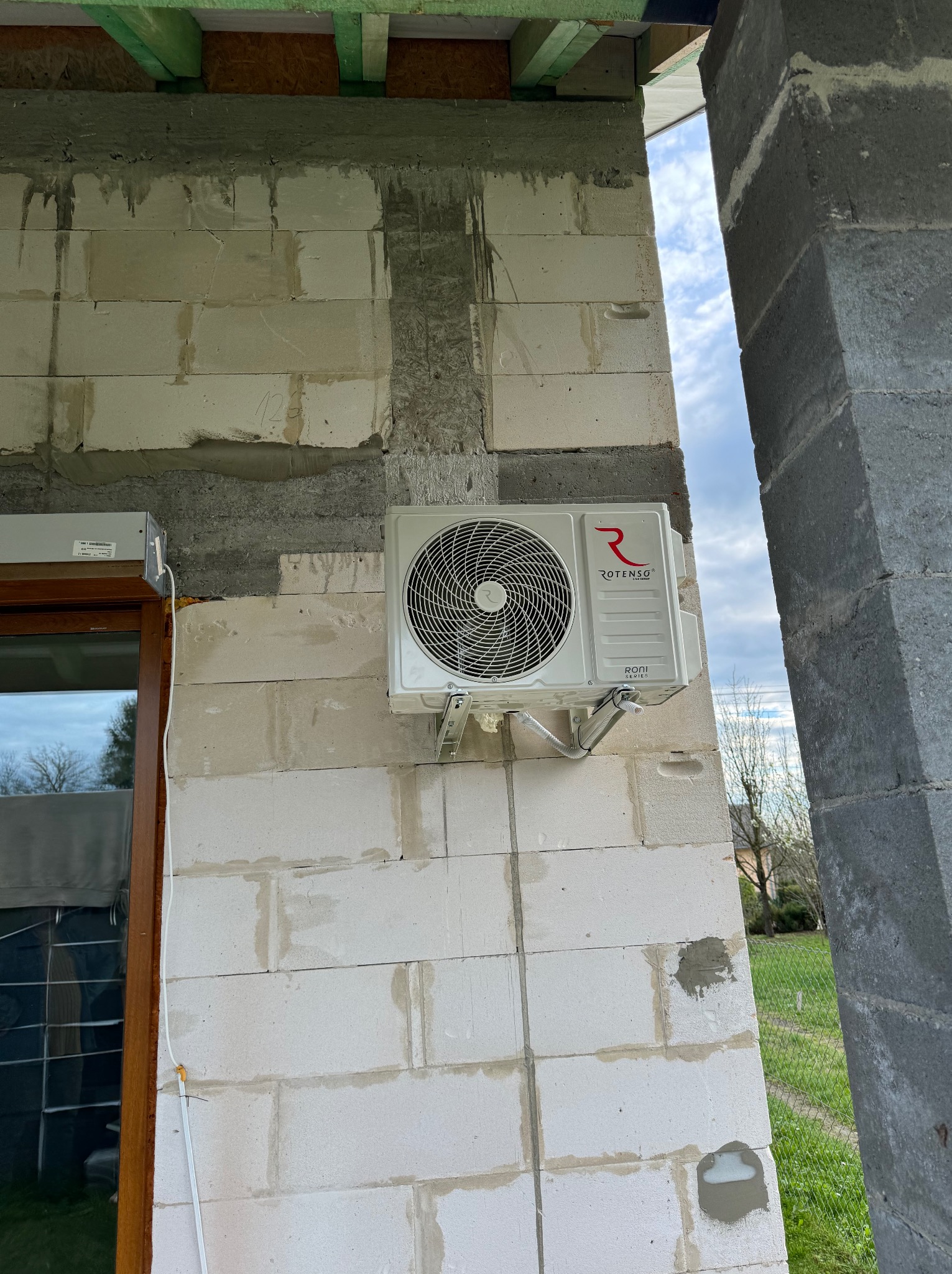Zewnętrzna jednostka klimatyzacji Rotenso zamontowana na ścianie z betonu komórkowego w trakcie budowy domu, widoczne elementy instalacji i przewody.
