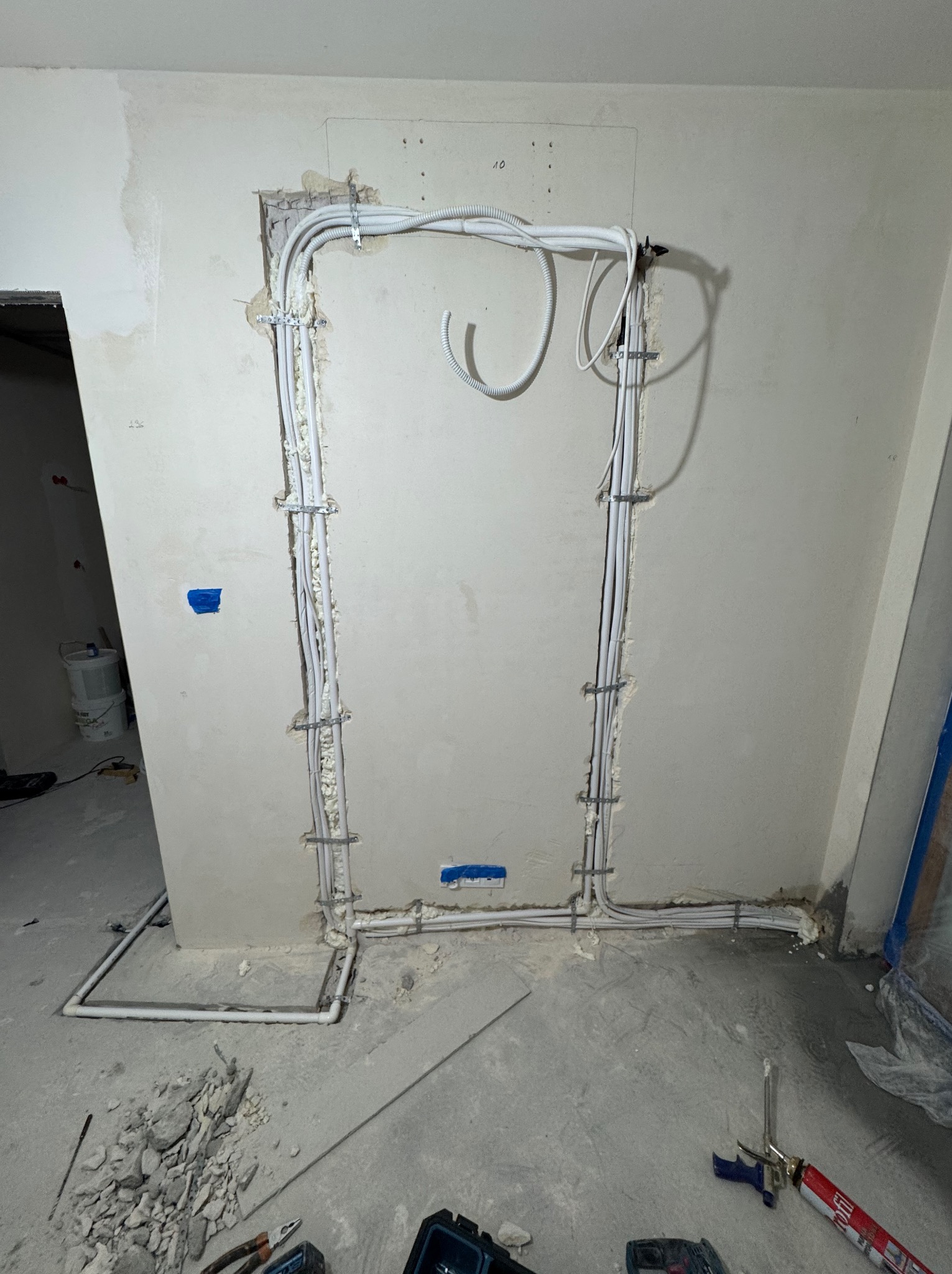 Montaż instalacji chłodniczej w ścianie, widoczne rury przymocowane do ściany pianką montażową i uchwytami. Na podłodze gruz i narzędzia.