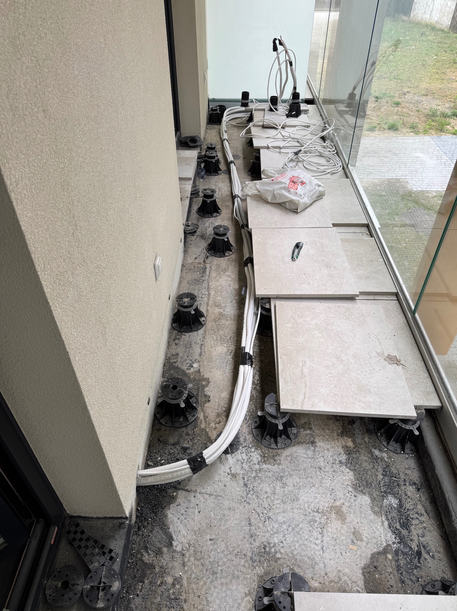 Montaż klimatyzacji: widok na podłogę z przewodami, wspornikami i płytami podłogowymi w trakcie instalacji, z oknem w tle i fragmentem ściany.