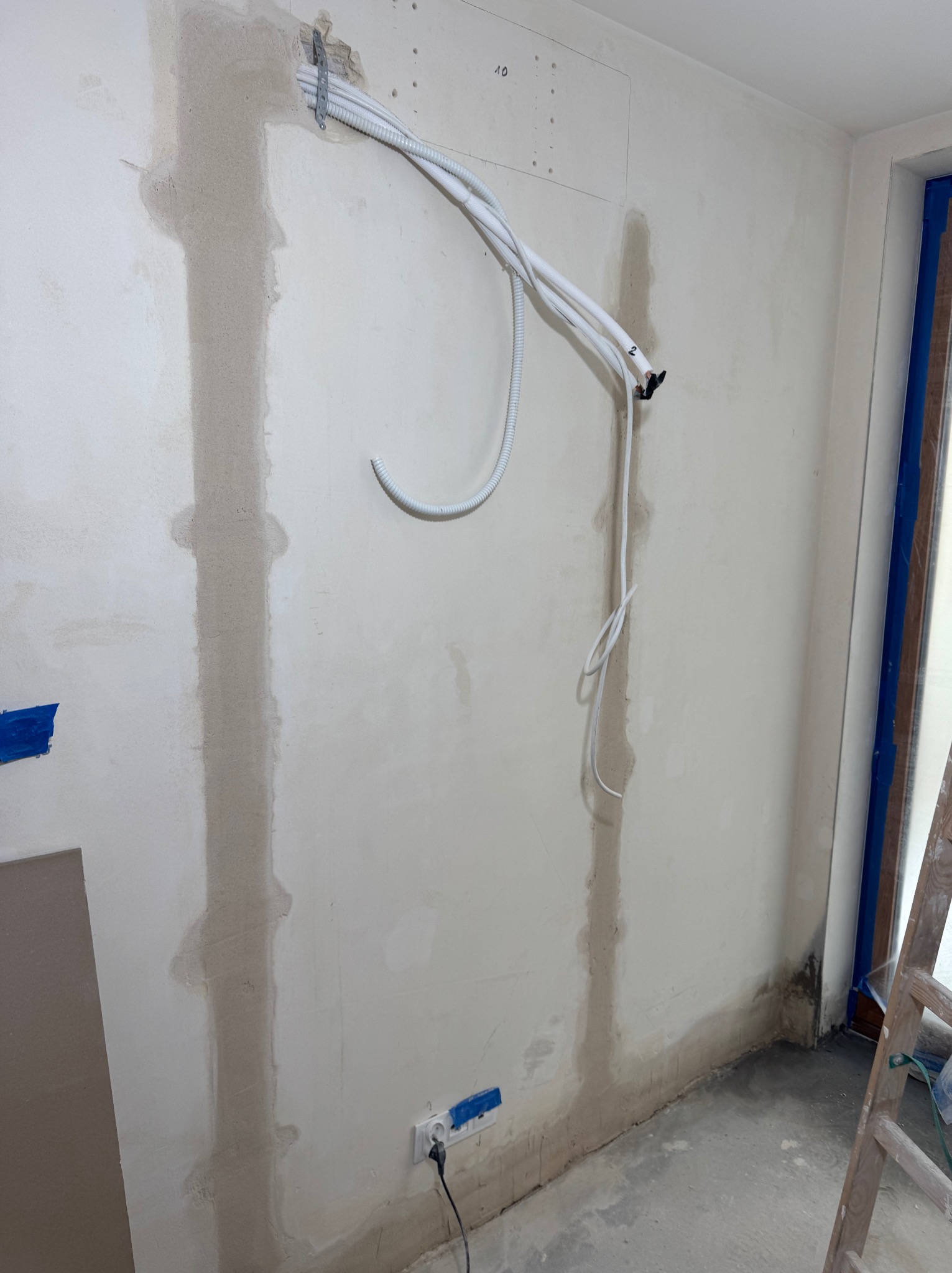 Instalacja przewodów klimatyzacji na ścianie w trakcie remontu. Widoczne kable, gipsowanie i przygotowanie do dalszych prac wykończeniowych.