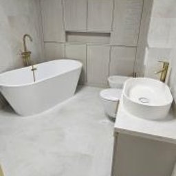 FORMAT MEBEL Henryk Rakowski - Nowoczesna łazienka z wolnostojącą białą wanną, złotą armaturą, podwieszaną toaletą i umywalką nablatową, wykończona jasnymi płytkami imitującymi kamień, z zabudową meblową pod sufit.