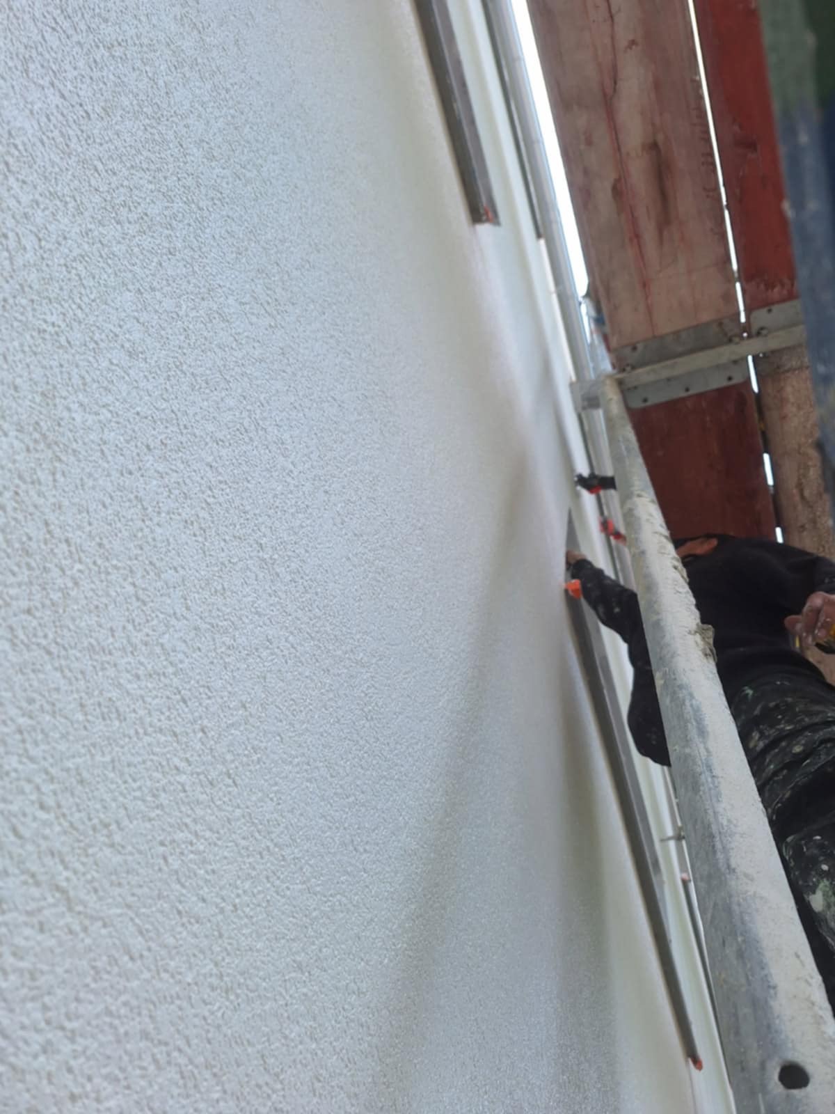 Tynkowanie elewacji budynku z rusztowania. Widoczna faktura świeżo nałożonego tynku baranka. Praca wykonywana przez pracownika w ubraniu roboczym.