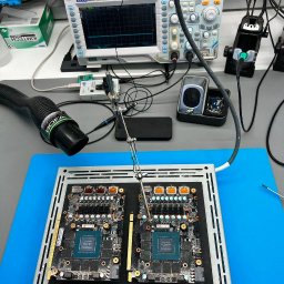 GadgetDoctor - Serwis Laptopów - Dwie karty graficzne w ramce, podłączone do sprzętu pomiarowego, z gumowymi rękami na oscyloskopie. Sprzęt do naprawy elektroniki.