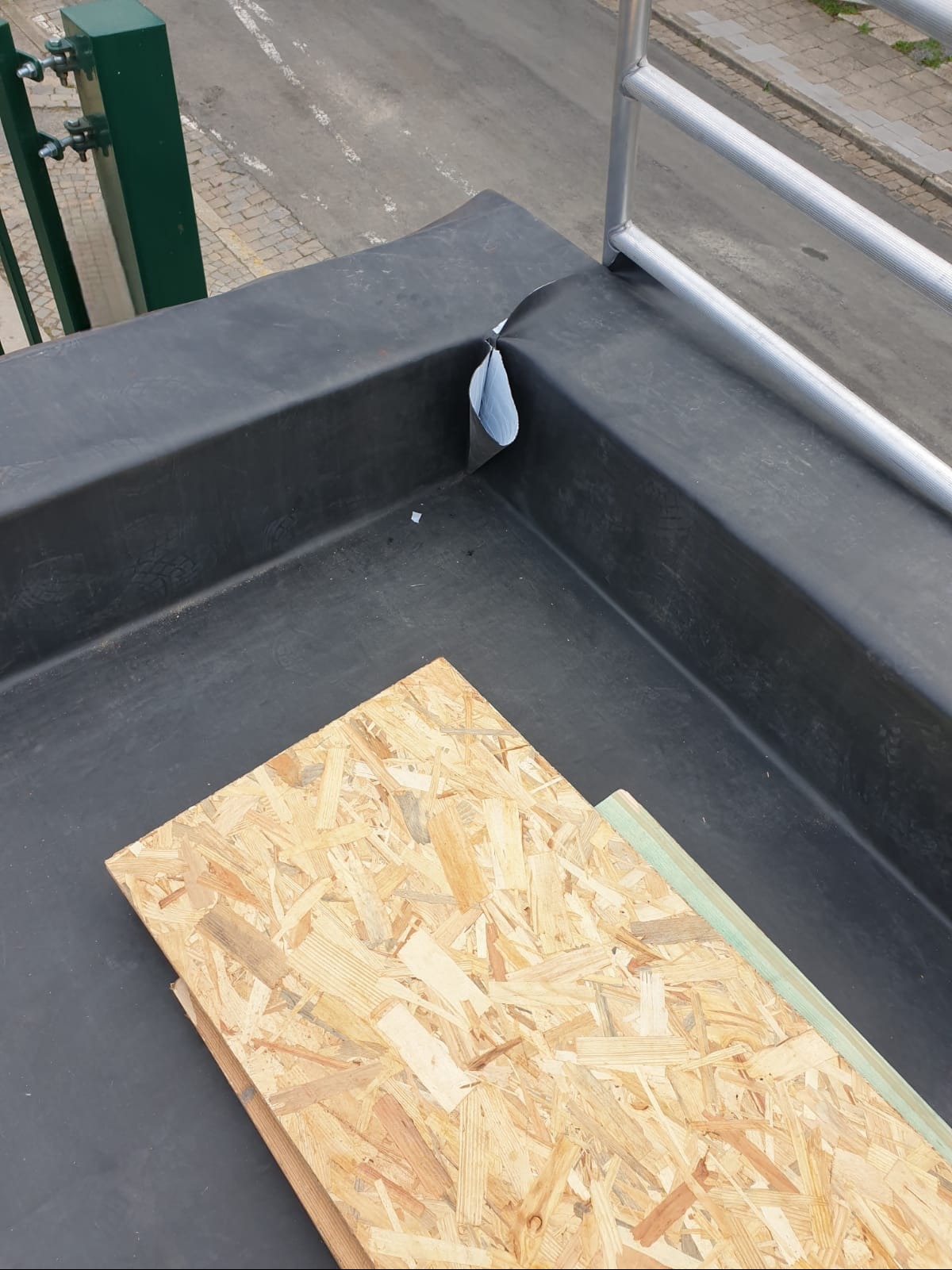 Fragment płaskiego dachu z czarną membraną hydroizolacyjną, widoczny fragment barierki ochronnej i przygotowane płyty OSB do dalszych prac.