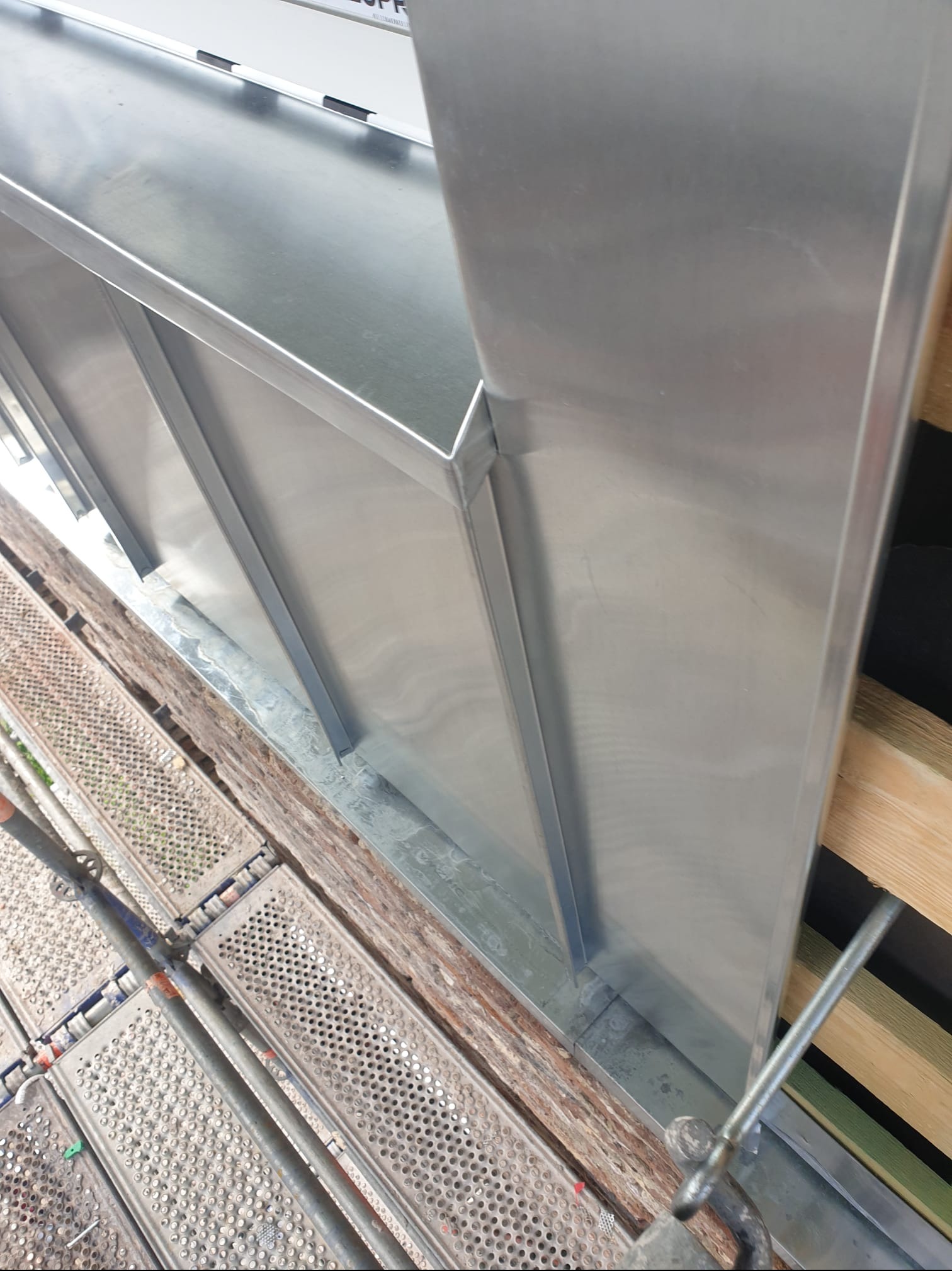 Metalowa obróbka blacharska okna dachowego z widocznymi elementami rusztowania i drewnianą konstrukcją dachu.