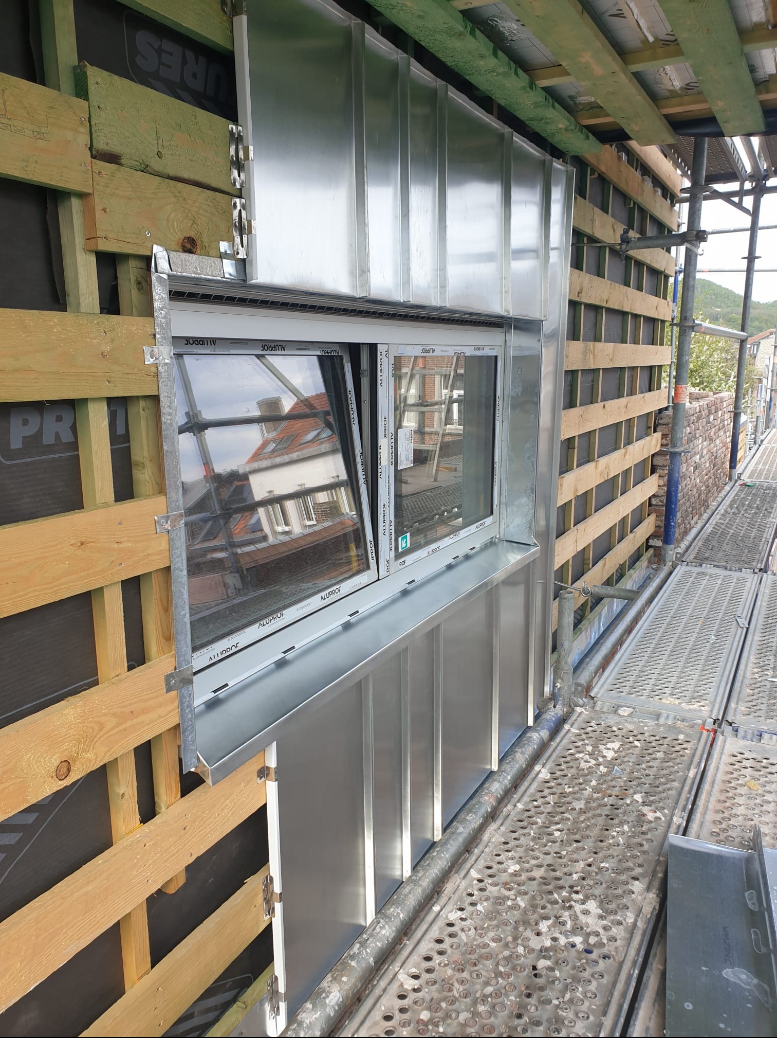 Montaż okna w nowej obudowie z blachy na elewacji budynku, widoczne rusztowanie i drewniana konstrukcja szkieletowa.